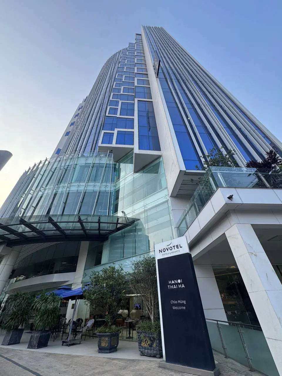 유리 외벽과 NOVOTEL HANOI THAI HA 표지가 보이는 호텔
