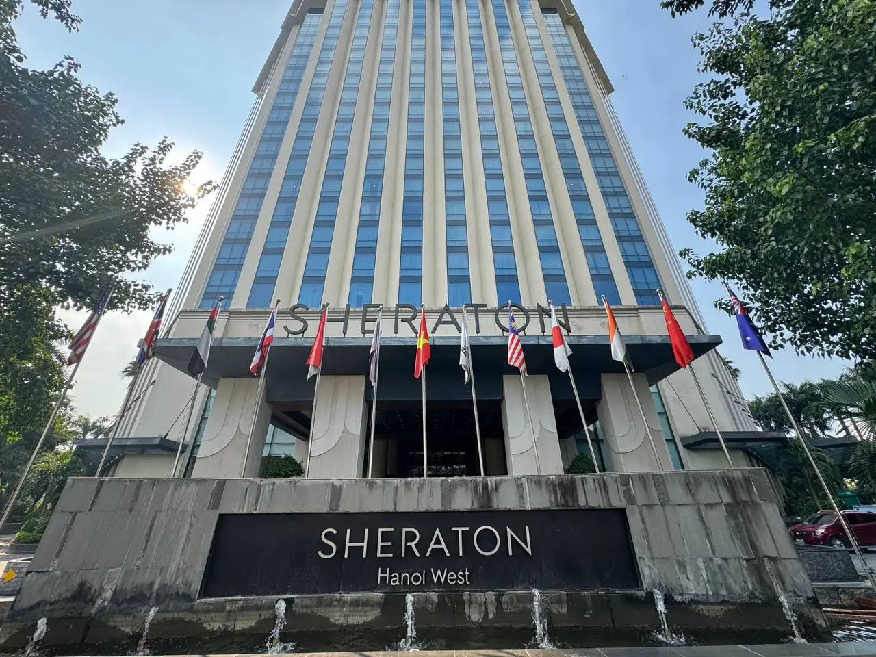 Sheraton Hanoi West 표지와 국기, 높은 건물이 보이는 쉐라톤 하노이 웨스트 정면